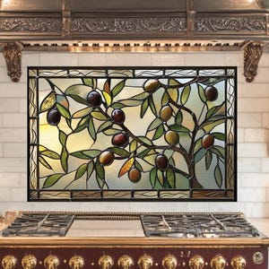 May include: Stained glass window featuring an olive tree design with green leaves and purple and green olives. The window is set in a black frame and mounted above a red and gold stove in a kitchen setting.