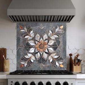 May include: A decorative kitchen backsplash featuring a floral design. The backsplash is made of tiles in shades of gray, white, and copper. The design is centered above a stainless steel range with a matching hood.