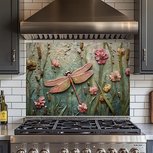 May include: A decorative kitchen backsplash featuring a 3D relief of a dragonfly and flowers. The artwork has a teal and green background with pink and yellow flowers and cattails. The dragonfly is a muted pink color.