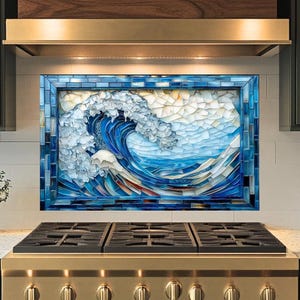 Op de afbeelding: Een mozaïeken achterwand met een grote oceaangolf in tinten blauw, wit en crème. Het kunstwerk is omlijst in een blauwe tegelrand en geïnstalleerd boven een gasfornuis. De keuken heeft groene kasten en een roestvrijstalen afzuigkap.