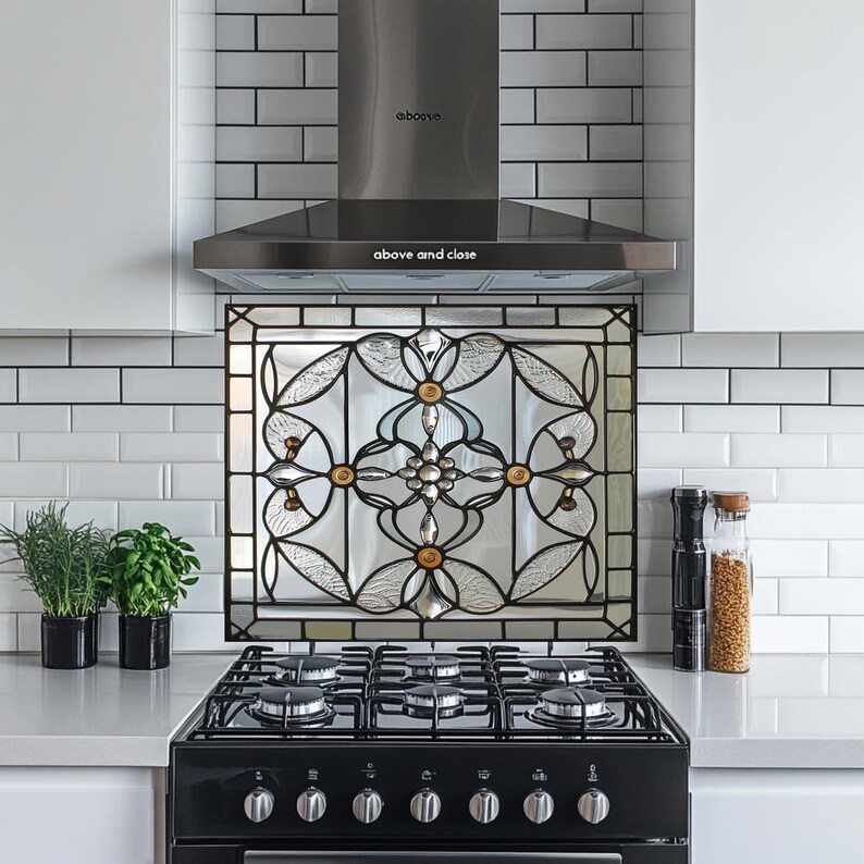 May include: A black and silver range hood above a black gas stove. A decorative stained glass panel with a floral design is mounted above the stove. The words "above and close" are printed on the range hood.