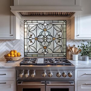 May include: A decorative stained glass kitchen backsplash with a black metal frame. The glass features a floral design with clear and textured glass, and gold and silver accents. The backsplash is installed above a stainless steel gas range.