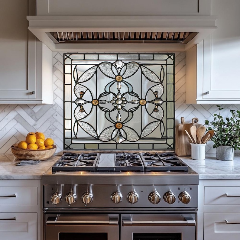 May include: A decorative stained glass kitchen backsplash with a black metal frame. The glass features a floral design with clear and textured glass, and gold and silver accents. The backsplash is installed above a stainless steel gas range.