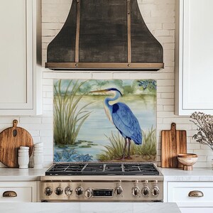May include: A decorative kitchen backsplash featuring a watercolor painting of a blue heron standing in a marsh. The artwork includes reeds, water lilies, and a serene lake scene, adding a touch of nature to the kitchen decor.