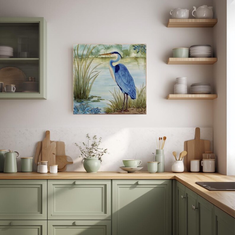 May include: A square canvas art print featuring a blue heron standing near a body of water. The artwork has a watercolor style with shades of blue, green, and brown. The heron is the focal point, with reeds and water lilies in the foreground.