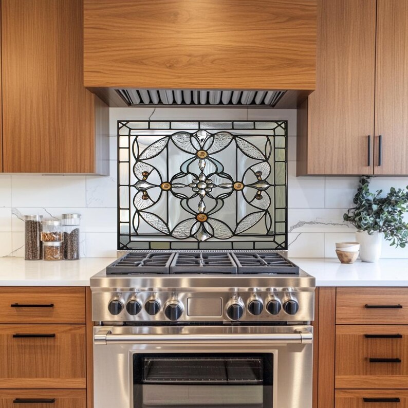 May include: A decorative stained glass backsplash with a floral design is installed above a stainless steel gas range. The glass features clear, amber, and black accents. The kitchen has wooden cabinets and a white countertop.