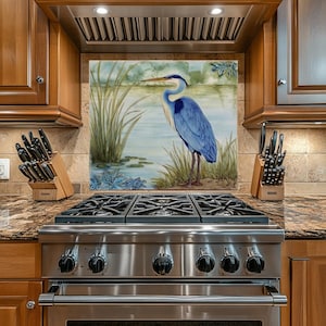 May include: A stainless steel gas range with six burners and a decorative backsplash featuring a blue heron standing in a marsh. The kitchen has wooden cabinets and a granite countertop.