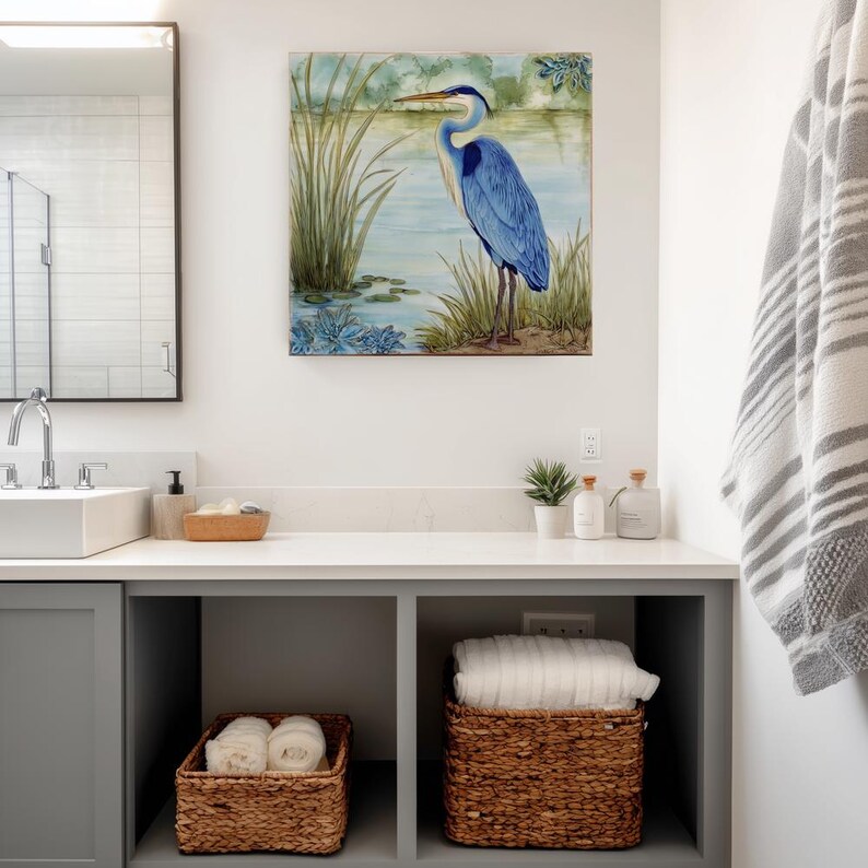 May include: A bathroom scene featuring a framed painting of a blue heron standing near a lake. The room includes a white countertop with a sink, a mirror, and woven baskets for storage. A gray and white striped towel hangs on the wall.