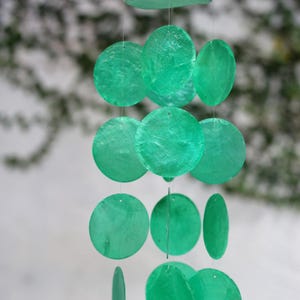 Peut inclure: Un carillon à vent en coquillages verts avec plusieurs disques ronds suspendus à une ficelle. Les disques sont de tailles différentes et sont disposés en cascade.