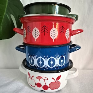 Pode incluir: Uma pilha de quatro panelas de esmalte com diferentes desenhos. A panela de cima é verde, a segunda é vermelha com um padrão de folhas brancas, a terceira é azul com um padrão geométrico branco e a panela de baixo é branca com um padrão de maçã vermelha e cereja.