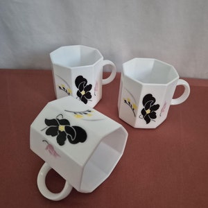 Peut inclure: Trois tasses en céramique blanche avec des motifs floraux noirs. Les tasses ont une forme octogonale et une poignée sur le côté droit.