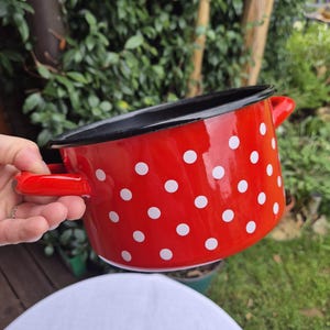 May include: Red enamel pot with white polka dots and black rim. The pot has two handles.