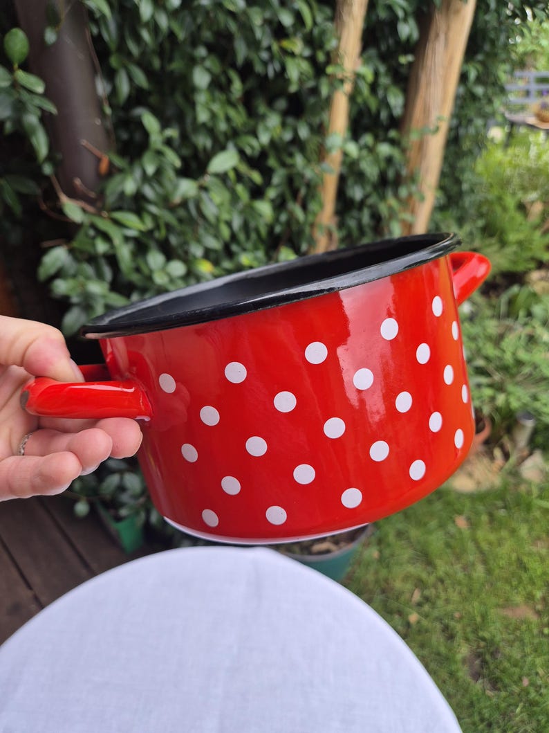 May include: Red enamel pot with white polka dots and black rim. The pot has two handles.