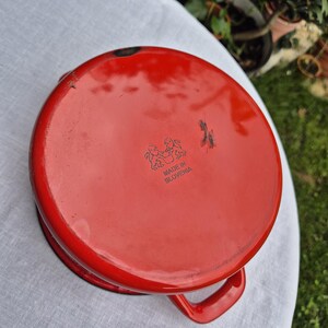 May include: Red enamel cast iron pot with a black handle and the words "Made in Slovenia" printed on the bottom.