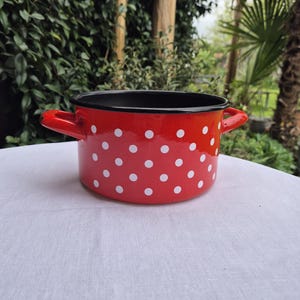 May include: Red enamel pot with white polka dots and black rim. The pot has two handles.