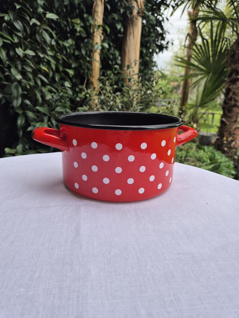 May include: Red enamel pot with white polka dots and black rim. The pot has two handles.