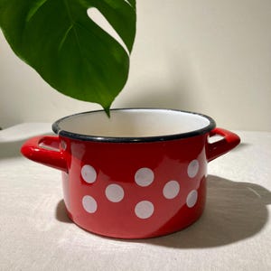 May include: Red enamelware pot with white polka dots and black trim. The pot has two handles.