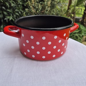 May include: Red enamel pot with white polka dots and black rim. The pot has two black handles.