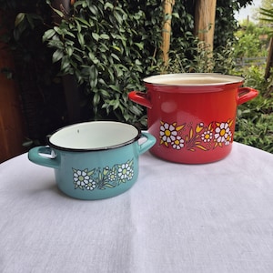 May include: Two enamel pots with floral designs. The larger pot is red with white flowers and yellow accents. The smaller pot is teal with white flowers and yellow accents.