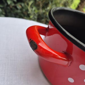 May include: Red enamel pot with white polka dots and a black rim. The pot has a single red handle.