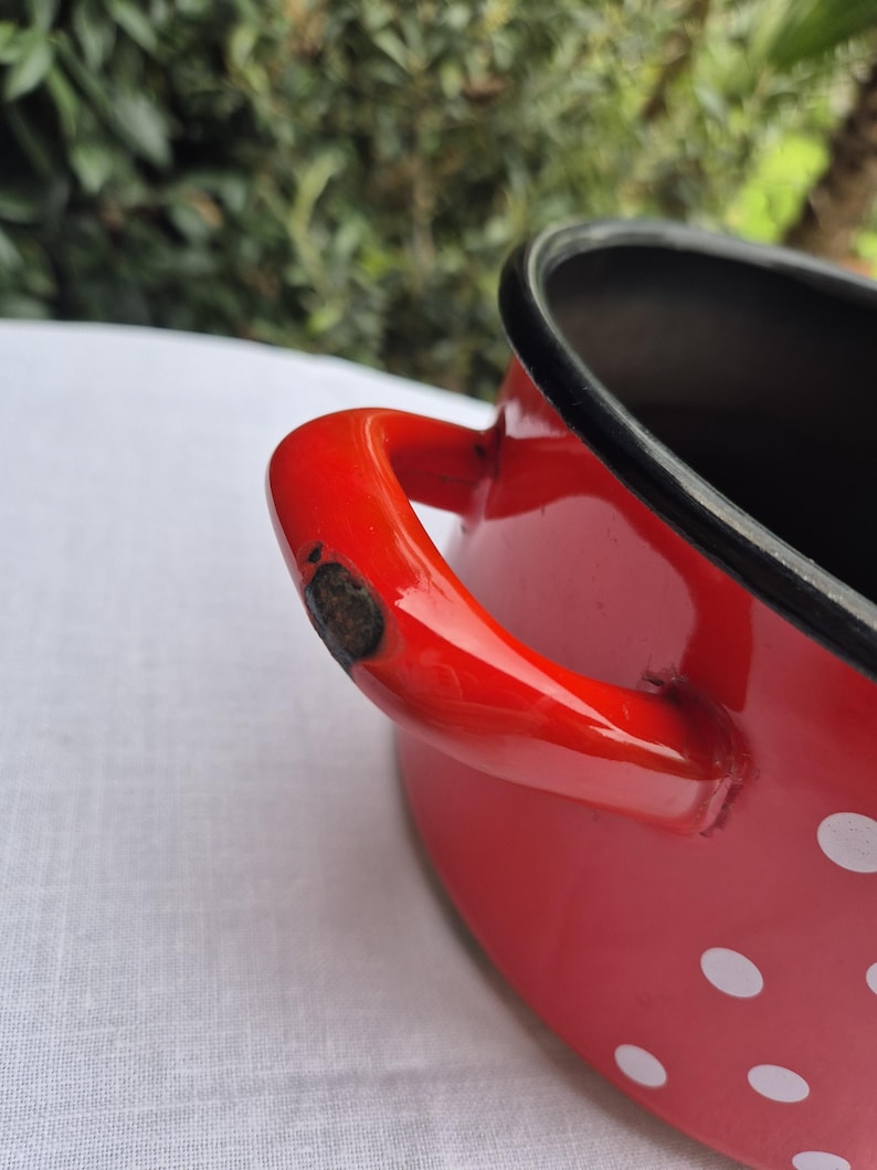 May include: Red enamel pot with white polka dots and a black rim. The pot has a single red handle.