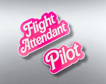 May include: Two pink and white stickers with the words "Flight Attendant" and "Pilot". The stickers have a retro design with a white outline and are set against a silver background. The stickers are likely for travel enthusiasts.