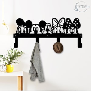 May include: Black metal wall-mounted coat rack featuring Mickey Mouse, Minnie Mouse, and Donald Duck silhouettes. The rack has four hooks and is decorated with a hat and a gray jacket. A decorative and functional item for any room.