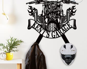 May include: Black metal motorcycle-themed wall art with the text "Kent's Garage". The art piece features a motorcycle design with flames and a banner. A black leather jacket and a white motorcycle helmet hang below.