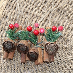 May include: Cinnamon sticks tied together with twine and decorated with red berries and green sprigs. The cinnamon sticks are arranged in a circular pattern.