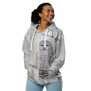 May include: A gray zip-up hoodie with a white owl illustration on the front. The owl is perched on a branch with a woodgrain background. The hoodie has a hood and a zipper closure.