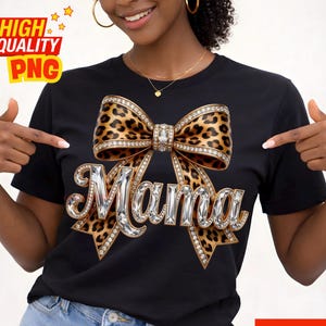 May include: Black t-shirt featuring a leopard print bow with rhinestone accents and the word "Mama" in a jeweled font. The shirt has a classic crew neck design and is made of a soft, comfortable material.