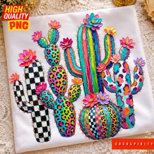 May include: A white t-shirt featuring a vibrant, textured graphic of multiple cacti. The cacti display colorful patterns including black and white checkers, neon leopard spots, and vertical stripes, all topped with bright pink, yellow, and purple flowers.