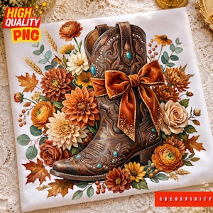 May include: A white t-shirt featuring a brown leather cowboy boot adorned with a large orange bow and turquoise accents. The boot is surrounded by a vibrant arrangement of autumn-colored flowers, including orange dahlias, yellow mums, and brown leaves.