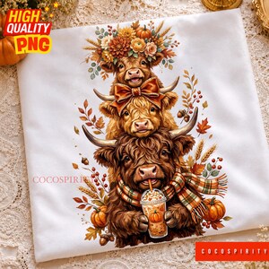May include: A white t-shirt featuring a graphic of three stacked Highland cows. The top cow wears a floral crown, the middle cow has a large bow, and the bottom cow wears a plaid scarf while holding a pumpkin spice latte. Autumn leaves, wheat, and pumpkins surround the cows.