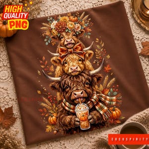 May include: A brown t-shirt featuring a graphic illustration of three stacked Highland cows. The top cow wears a floral crown, the middle cow has a bow, and the bottom cow wears a plaid scarf while holding a pumpkin-themed iced coffee cup.