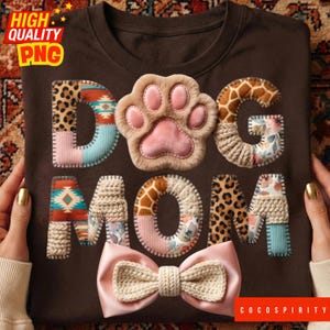 May include: A brown t-shirt with the text "DOG MOM" in a patchwork style. The letters incorporate various patterns, including leopard print, a dog paw, and giraffe print. A pink bow is at the bottom.