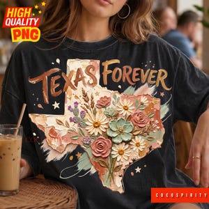 Pode incluir: Camiseta preta com um design floral do estado do Texas e as palavras "Texas Forever". O design inclui um mapa do Texas preenchido com flores em tons de rosa, verde e creme. A camiseta tem um visual vintage.