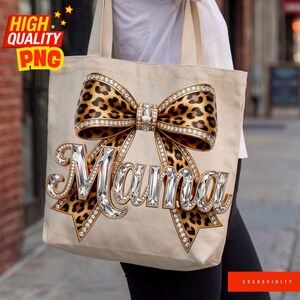 May include: Beige tote bag featuring a large leopard print bow embellished with rhinestones. The word "Mama" is spelled out in sparkling, jewel-like letters. The bag has a simple design with a focus on the decorative bow.