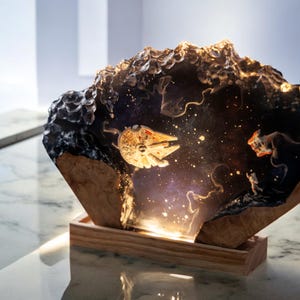 Könnte beinhalten: Eine Harzskulptur eines Raumschiffs, das durch eine Galaxie fliegt, auf einem Holzsockel. Das Raumschiff ist ein Millennium Falcon, und die Galaxie ist gefüllt mit Sternen und Nebeln.