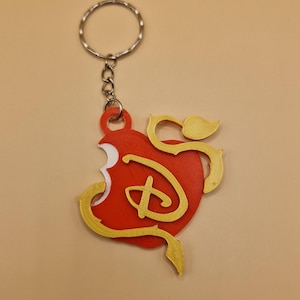 May include: A red and gold heart-shaped keyring with a stylised "D" inside. The keyring is attached to a silver key ring.