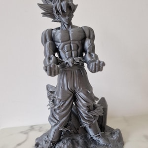 Peut inclure: Une figurine en plastique gris imprimée en 3D d'un personnage de l'anime Dragon Ball Z. Le personnage est debout, les bras tendus, avec une expression déterminée sur le visage. La figurine est détaillée et réaliste, avec une définition musculaire visible et des vêtements texturés.
