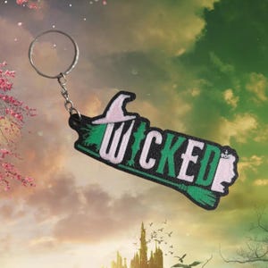 May include: A green and black keychain with the word "WICKED" in white letters. The keychain features a witch's hat and a broom.