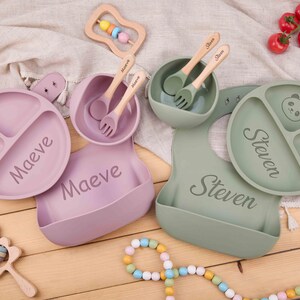 Peut inclure: Ensemble d'alimentation pour bébé en lavande et vert sauge. Comprend des assiettes compartimentées, des bols, des bavoirs, des cuillères et des fourchettes personnalisés. Des hochets en bois et un collier de perles complètent l'ensemble.