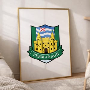 Puede incluir: Una impresión enmarcada con el escudo de armas de Fermanagh, que muestra un castillo amarillo sobre un escudo verde con un fondo ondulado azul y blanco y una cruz roja, con la palabra FERMANAGH impresa en blanco en una cinta verde abajo.