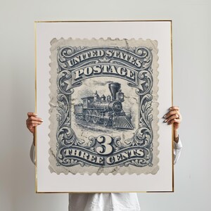 May include: A framed print of a vintage United States postage stamp. The stamp features a detailed illustration of a steam train and the text "UNITED STATES POSTAGE" and "THREE CENTS" in a decorative frame. The print has a gold frame.