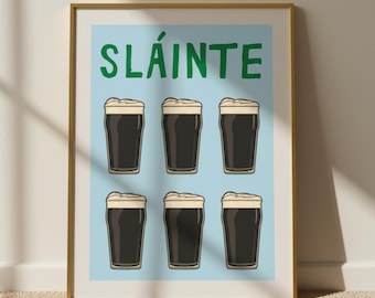 May include: A framed print featuring six pints of dark stout with creamy foam, set against a light blue background. The word "SLÁINTE" is printed in green at the top. The artwork is in a gold frame.