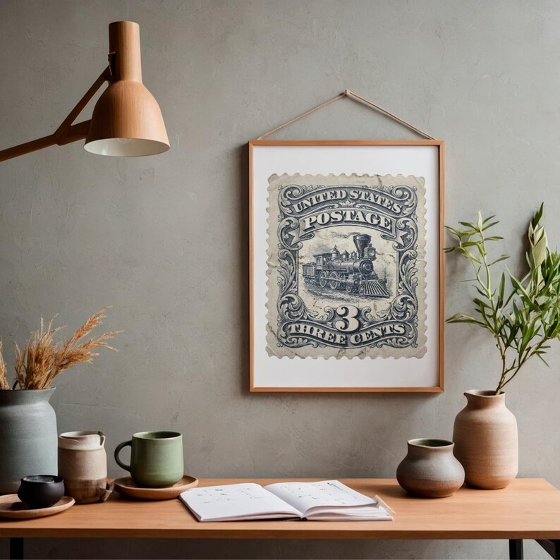 May include: Framed vintage postage stamp print featuring a detailed illustration of a steam train. The stamp is in shades of blue and white, with the text "UNITED STATES POSTAGE" and "THREE CENTS". The print is displayed in a wooden frame, hanging on a gray wall.