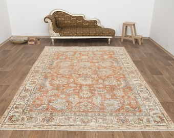 Op de afbeelding: Een rechthoekig, antiek tapijt met een verweerd bloemenpatroon in oranje, crème en blauw. Het tapijt ligt op een houten vloer, met een chaise longue en een kleine houten kruk op de achtergrond. Afmetingen ca. 240 cm x 300 cm.