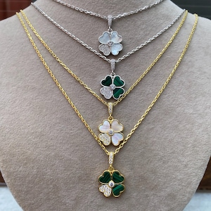 May include: Four gold necklaces with four-leaf clover pendants. The pendants are made of white mother of pearl, green malachite, and clear crystals.