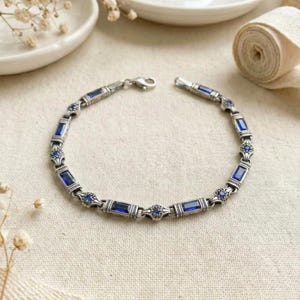 May include: Silver bracelet with rectangular and round blue gemstones. The bracelet is made of silver and features a clasp closure. The gemstones are a deep blue color and are set in a decorative pattern.